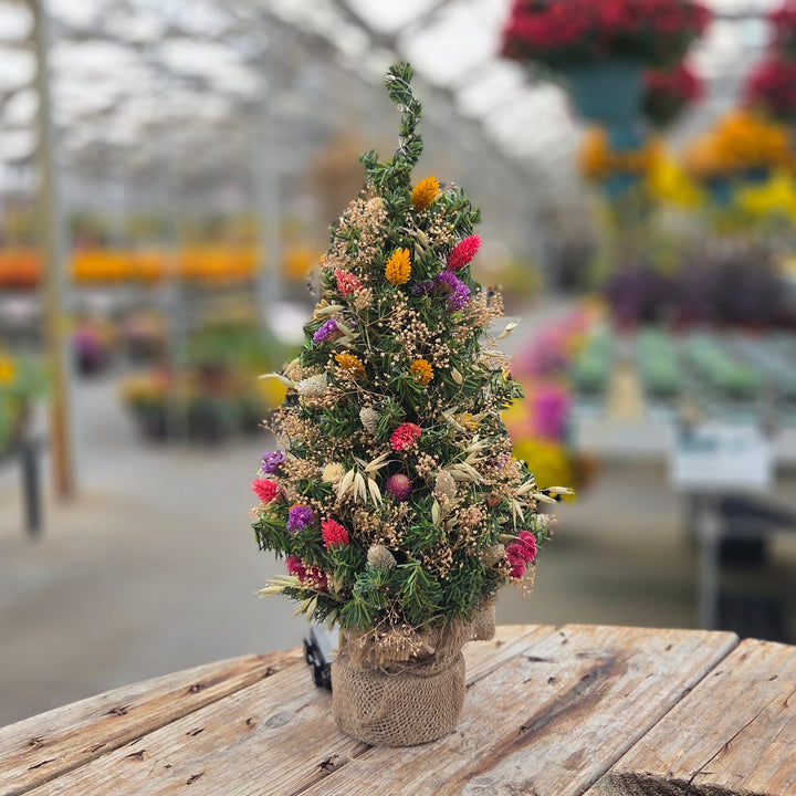 Small potted tree with colorful flowers on a wooden table in a greenhouse setting.